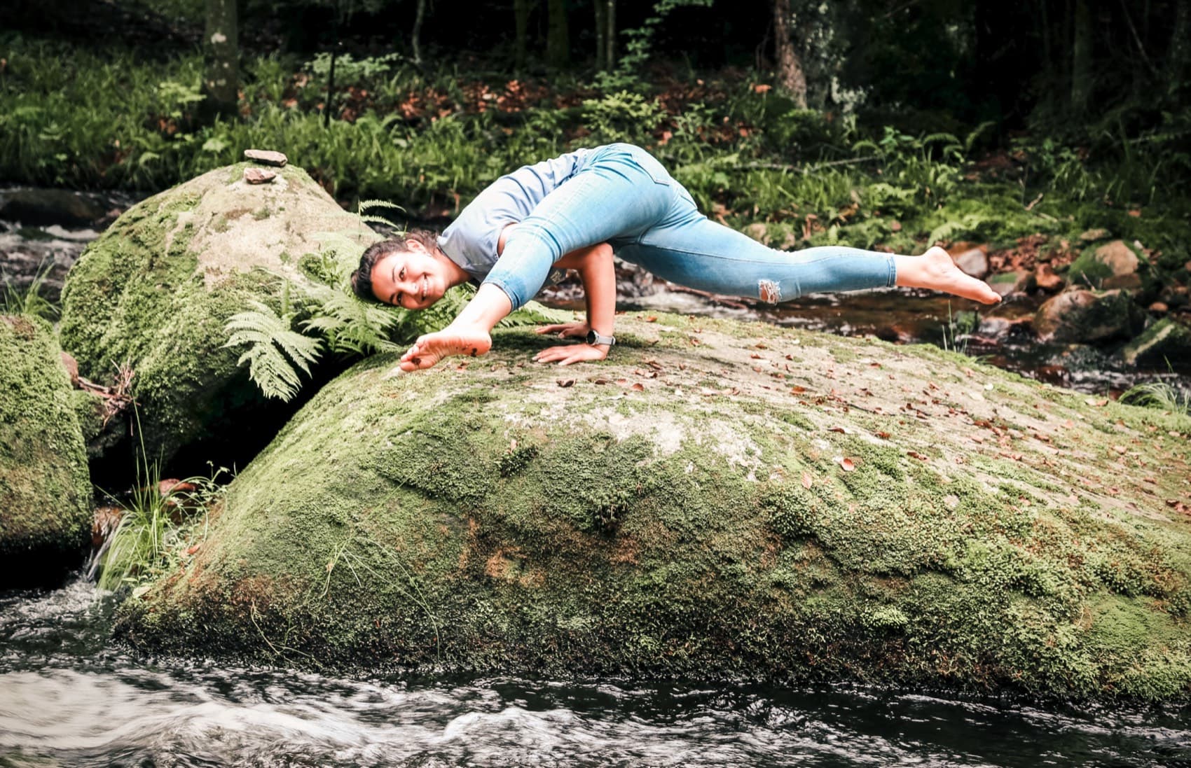 Sophie balanciert in einer Yoga-Pose auf einem moosbewachsenen Stein am Bach