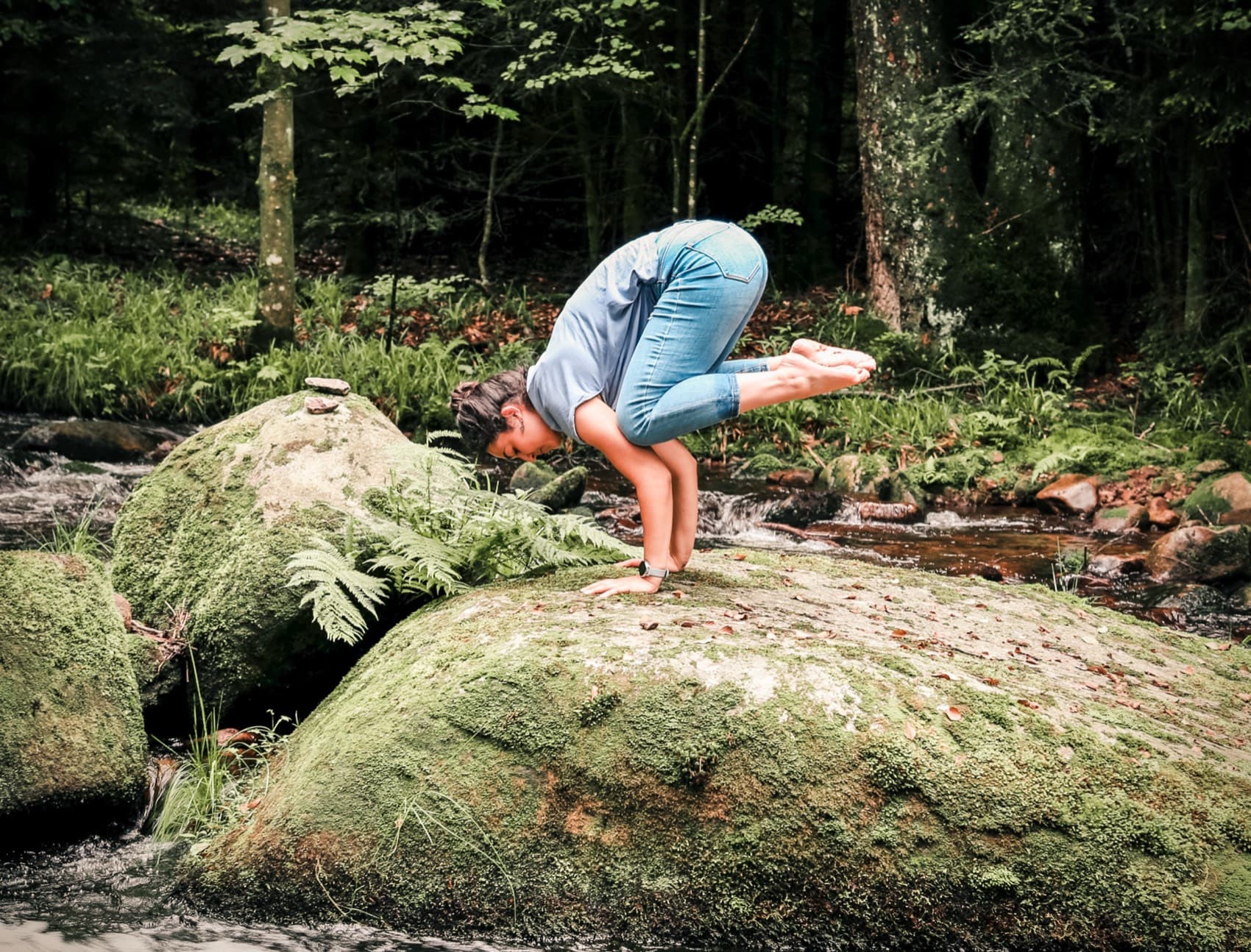 Sophie in der Krähe (Bakasana) auf einem Felsen im Wald